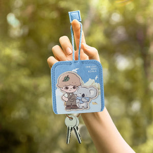 DIMOO ONE DAY WITH KOALA SERIES blue key case featuring whimsical character design displayed in outdoor setting. Collectible blind box accessory with practical keychain functionality.