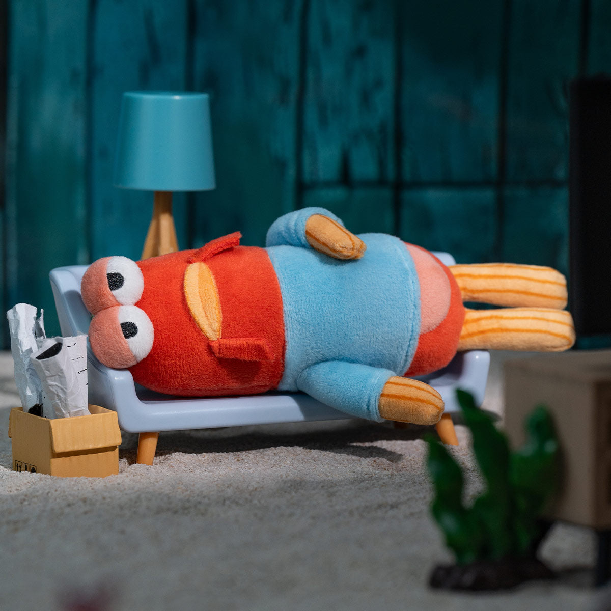 Large limp fish plush figure lying on white chair in living room setting with lamp and plant.
