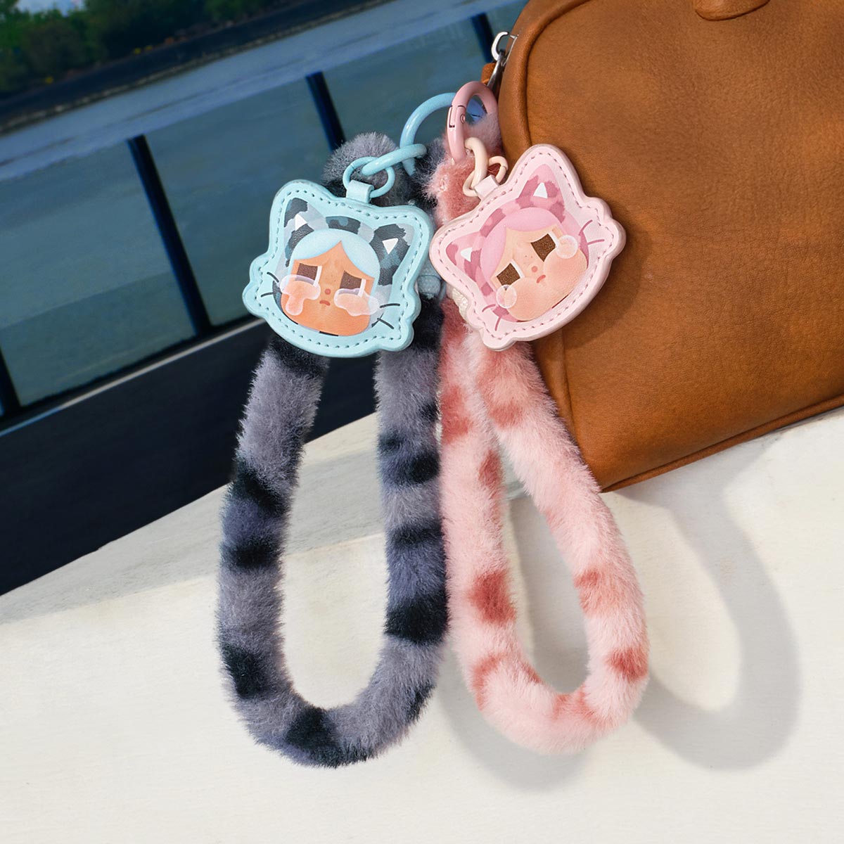 Two CRYBABY Wild but Cutie Series plush keychains attached to a tan/brown handbag, photographed in what appears to be a car interior. 