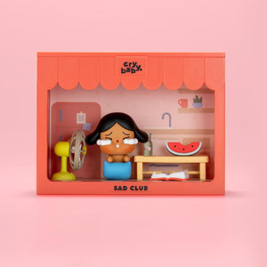 CRYBABY Sad Club Series bedroom scene set with pink background featuring detailed miniature furniture and emotional character. Collectible diorama with intimate storytelling elements.